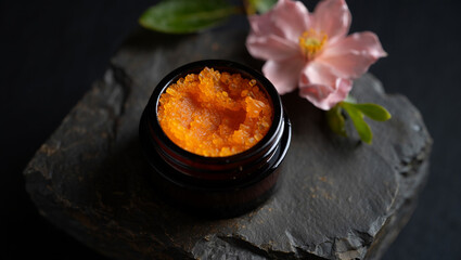 Close up of orange caviar in a small jar with a pink flower and green leaves