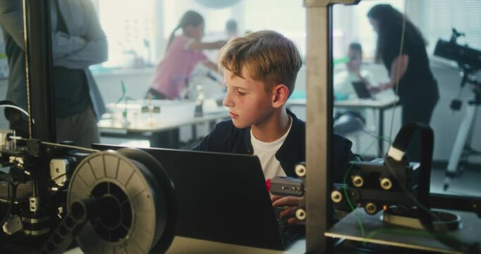 Elementary School Student Writing Code for Advanced Automated 3D Printer on Laptop During Programming Lesson. Smart Young Boy Studying Technology in Modern Classroom. Interactive STEM Education.