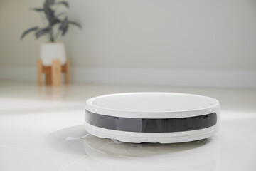 White automatic floor cleaner with side brush on tile flooring, featuring front black sensor strip....
