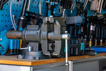 metal bench vise mounted on a wooden workbench in a workshop, with hand tools and power tools...