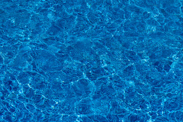 Background and texture of clear blue water with sunlight reflections in a swimming pool. A fresh, summer-themed visual perfect for graphic design projects.