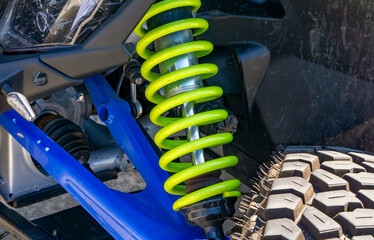 off-road vehicle suspension system, featuring a bright green coil spring, blue control arms, and a...