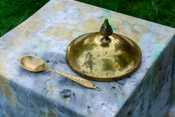 brass spoon and an ornate lid with an oriental-style handle placed on a marbled surface, with green...