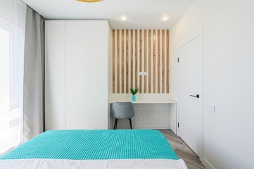 modern bedroom with a turquoise bedspread. It features white walls, a wardrobe, a wooden slat...