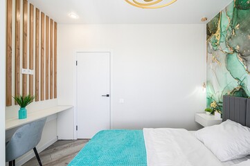 modern bedroom featuring a bed with a turquoise blanket, white walls, wood accents, a desk, and an...