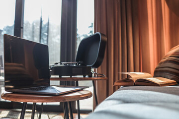 Fototapeta premium Laptop on a small round table with a turntable and open book in the background, set in a cozy interior with warm sunlight and curtains
