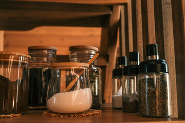 Close-up of a wooden kitchen shelf with glass jars filled with coffee, sugar, tea, and spices....