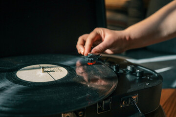 Close-up of hand placing needle on vinyl record on turntable, cozy warm lighting and shallow depth of field enhance vintage atmosphere