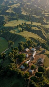 Aerial view of lush green hills with scattered trees and a small village, captured in a cinematic video style from a high-angle perspective. Live mobile wallpaper.