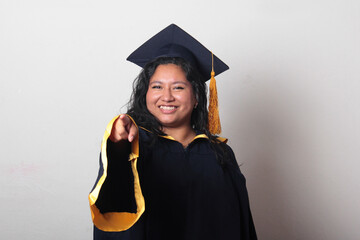 Young brunette Latina woman wearing a cap and gown celebrates her graduation and the completion of...