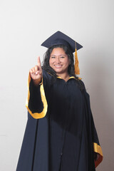 Young brunette Latina woman wearing a cap and gown celebrates her graduation and the completion of...