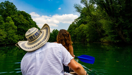 wo travelers explore a tranquil river by canoe under a clear sky, dressed for sun protection and...