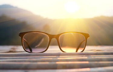 Eyeglasses on wooden table with sun light and mountain background.