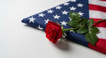 A red rose placed gently beside a folded U.S. flag, photographed on an isolated white background.