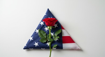 A red rose placed gently beside a folded U.S. flag, photographed on an isolated white background.