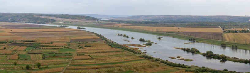 Panoramic view of a wide river winding through fertile agricultural fields under a vast sky,...