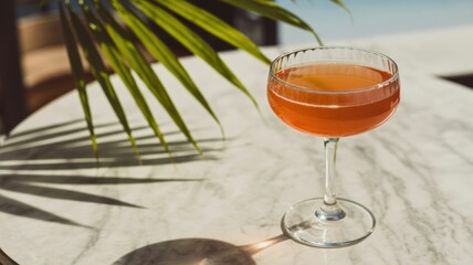Refreshing cocktail in elegant glass on marble table by the beach with tropical palm shadow