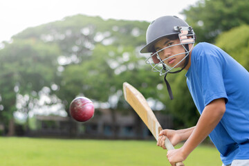 A teenage boy wearing a blue shirt and helmet holding a cricket bat, playing and hitting cricket ball on a school field. He looks focused and ready for action, in motion, selective focus on boy.