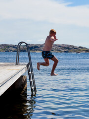 A young boy jumping from a pier in to the water a clear sunny summer day
