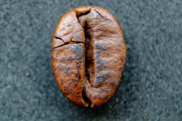Naklejka premium A crisp and detailed closeup shot of a roasted coffee bean displaying its natural texture and deep brown color on a dark gray surface