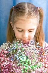Portrait of Little Girl with Ponytails. She is Sniffing a Bouquet of Colorful Gypsophila Flowers.