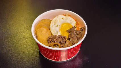 Delicious beef bibimbap bowl with fried egg and kimchi ready to eat on dark surface