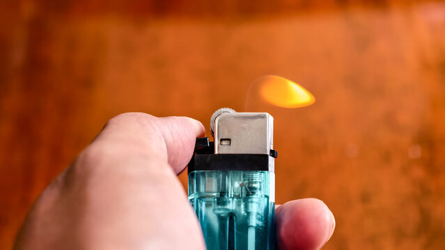 Hand Holding a Blue Lighter with a Dancing Flame against Wood Backdrop