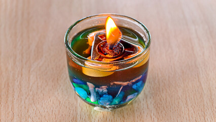 Unique gel candle in a glass filled with colorful liquid and decorative stones on wooden table