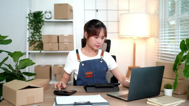 Home based businesswoman using tablet and laptop to handle online orders surrounded by eco packaging and supplies