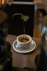  A close-up shows a thin stream of liquid pouring from a curved spout into a white ceramic cup on a...