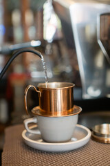 Copper Vietnamese coffee filter sitting on a white cup and saucer