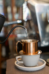 Copper Vietnamese coffee filter sitting on a white cup and saucer