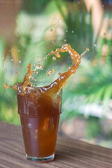 Splash of cola drink with ice in a glass with green blurred background