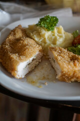 Chicken Kiev. Breaded and fried chicken fillets on a white plate, accompanied by creamy mashed potatoes garnished with fresh parsley.