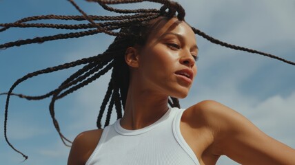 Young african female with braided hair in white tank top under blue skies