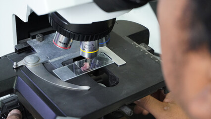 Close-up view of a scientist using a compound microscope to observe a sample slide in the laboratory.
