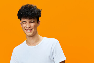 smiling young man with curly hair in white t-shirt expressing joy on vibrant orange background,...