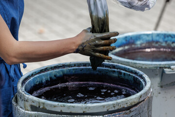 Bean sized indigo blue droplet falls from pinky of artisan's dye soaked hand as it wrings out a...