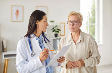 Professional doctor in white coat discussing results of medical tests with older female patient in...