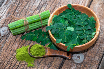Moringa leaves in wooden bowl with Moringa powder on wooden background