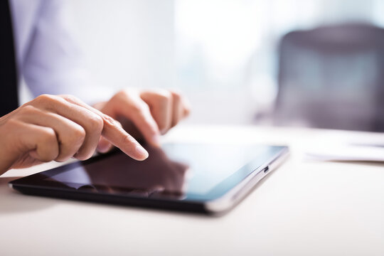 man using digital tablet at office desk, close-up of hands touching screen. Modern technology, business communication, online work, wireless device, workplace, professional lifestyle, innovation.