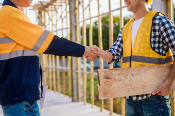 An elderly engineer and a middle-aged man shake hands at a construction site, symbolizing mutual...