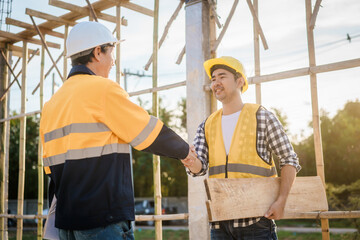 An elderly engineer and a middle-aged man shake hands at a construction site, symbolizing mutual...