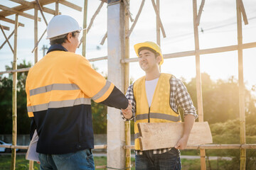 An elderly engineer and a middle-aged man shake hands at a construction site, symbolizing mutual...