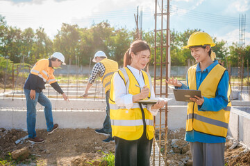 An elderly engineer, a middle-aged man, and two young Asian women at construction site, wearing...