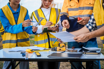 At a table on a construction site, an elderly male safety expert, a middle-aged man, and two young...