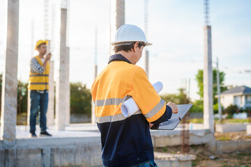 An Asian middle-aged male engineer wearing a yellow safety helmet and reflective vest uses a...