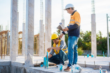 An elderly man and a middle-aged Asian man, both wearing hard hats and reflective vests, closely...
