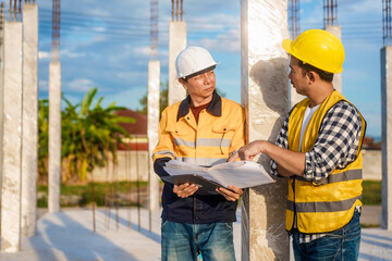 An elderly man and a middle-aged Asian man, both wearing hard hats and reflective vests, closely...