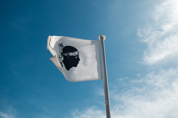The Moors head of the Corsican flag fluttering in the wind on a flagpole against a deep blue sky